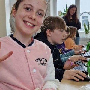 Girl smiling at camera. Children on computers in the background. 